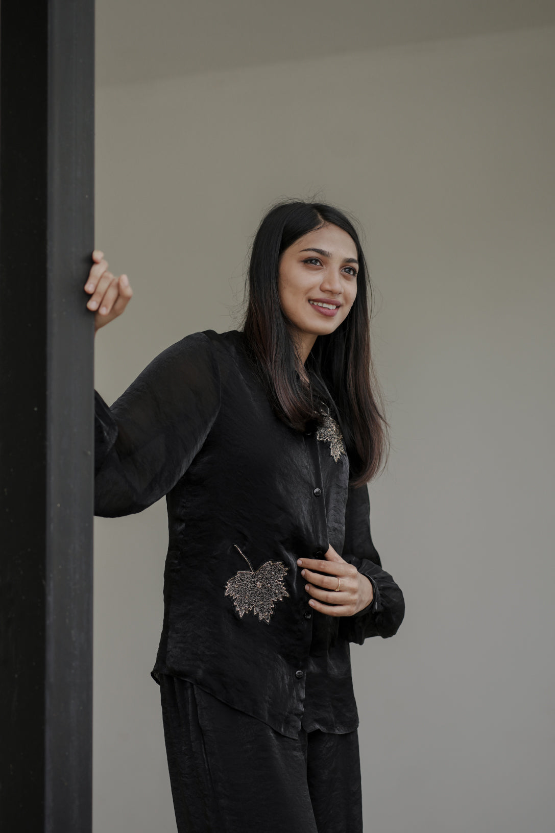 Woman wearing Noira black co-ord set with leaf handwork on the shirt, standing against a plain background