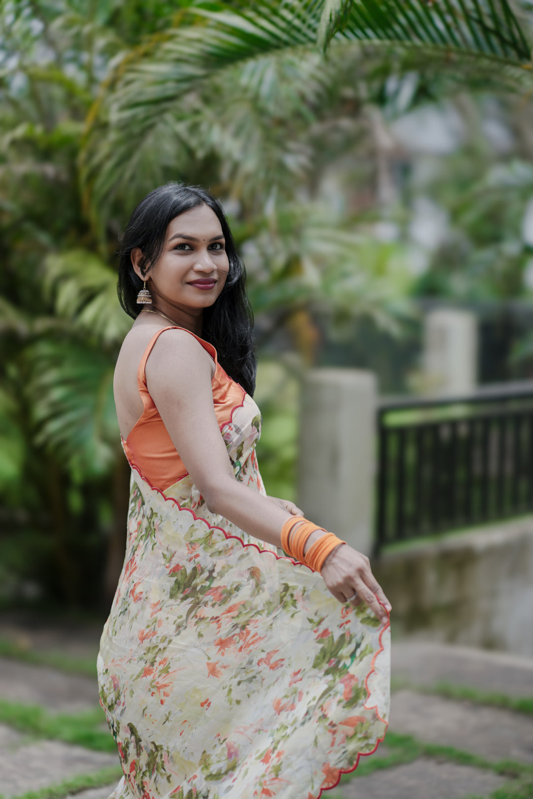 Woman wearing Elaria saree in light yellow with orange digital floral print standing outdoors with palm tree background