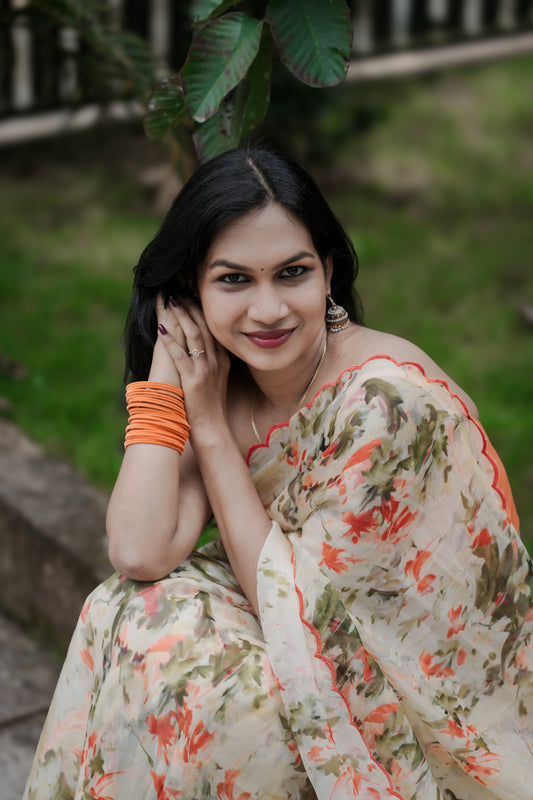 Elaria premium organza saree in light yellow with orange digital floral print sitting outdoors with greenery