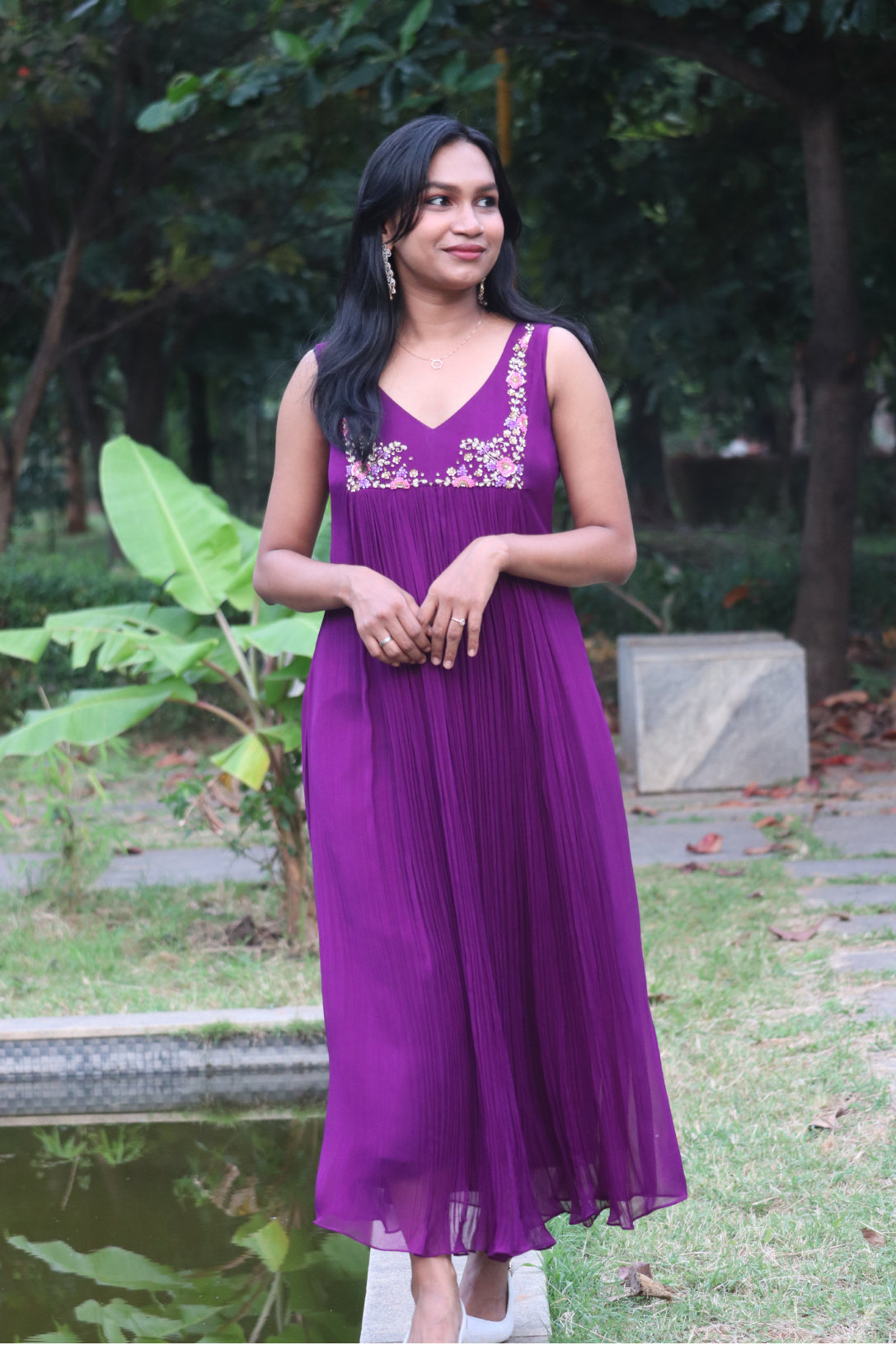 Woman wearing Viola dark purple viscose georgette kurti with handwork embroidery, standing near a pond with trees in background