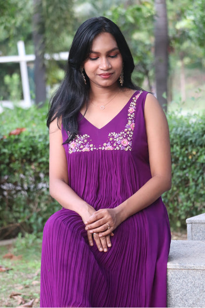 Woman wearing Viola dark purple viscose georgette kurti with handwork embroidery, sitting on a stone ledge outdoors, hands folded